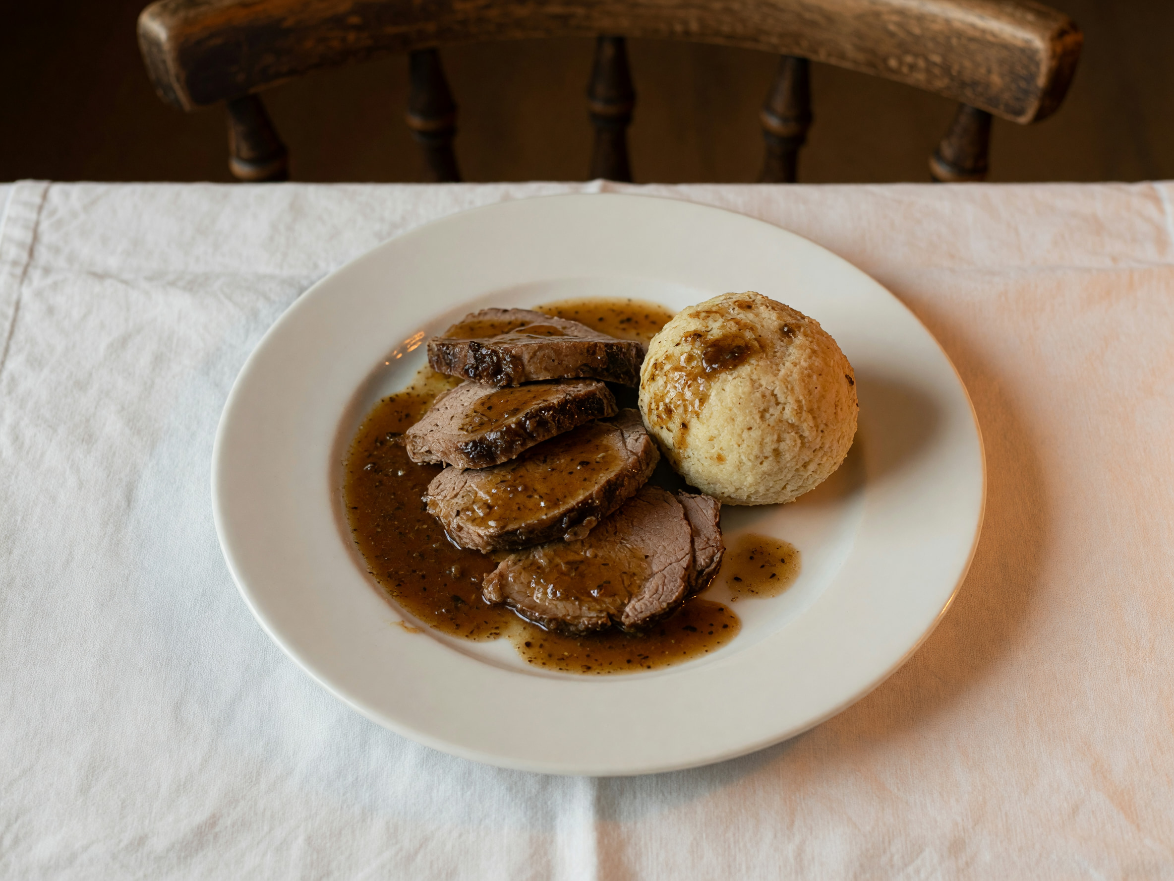 Üppiger Wiener Bratenklassiker mit Knödel und dunkler Sauce auf weißem Teller im warmen Wirtshauslicht
